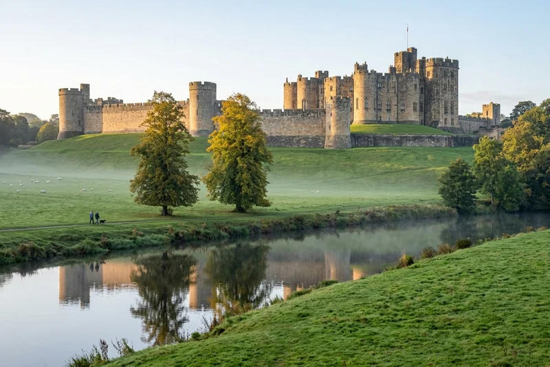 Alnwick Castle above misty parkland and the River Aln at sunrise, with grazing sheep