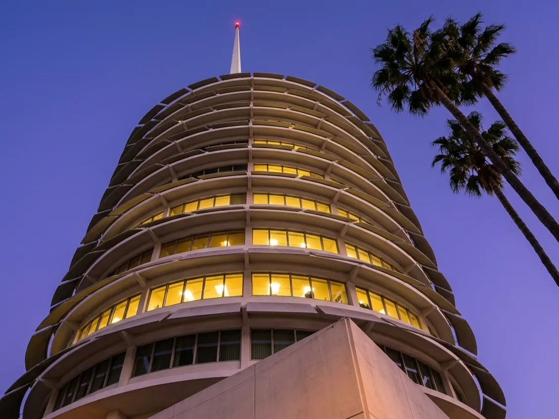 The round Capitol Records tower in Hollywood at dusk, its windows lit, with two palms