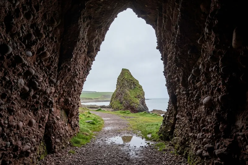 Looking out through the arch of the Cushendun Caves toward a grassy sea stack
