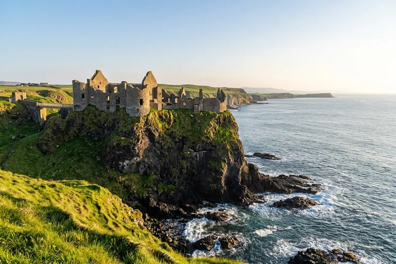 The ruins of Dunluce Castle on a green clifftop above the sea in County Antrim