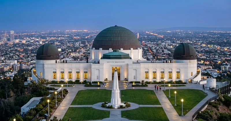 Griffith Observatory and its lawn with the obelisk above the lights of Los Angeles at dusk