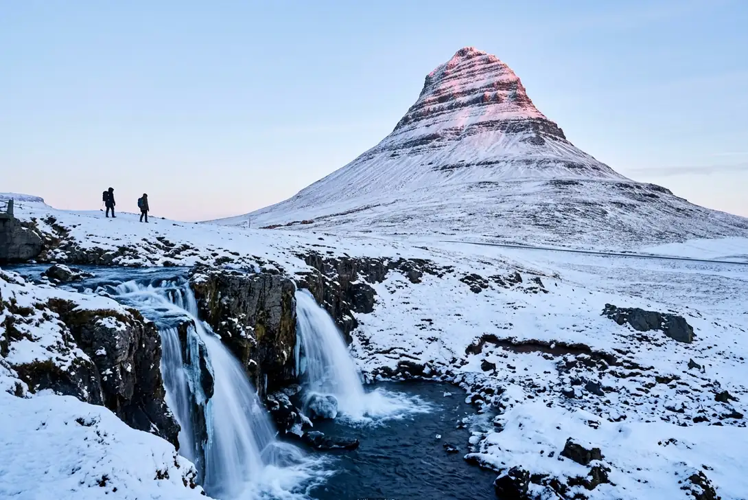 Snow-covered Kirkjufell above the half-frozen Kirkjufellsfoss falls near Grundarfjörður, two hikers on the ridge