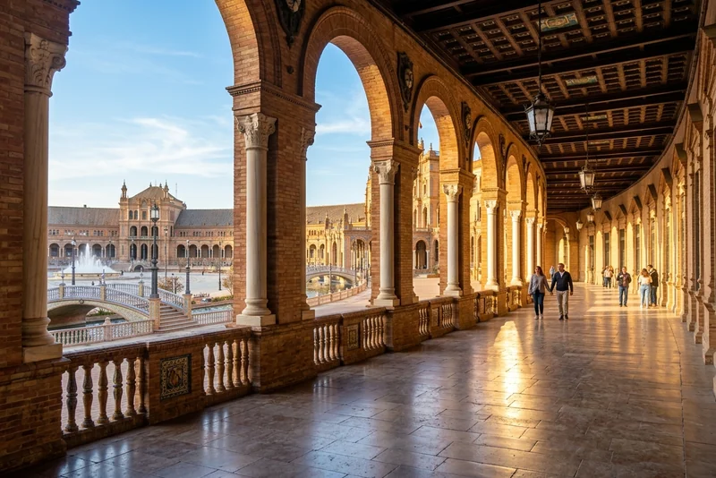 A sunlit brick arcade of the Plaza de España in Seville, looking out to the canal