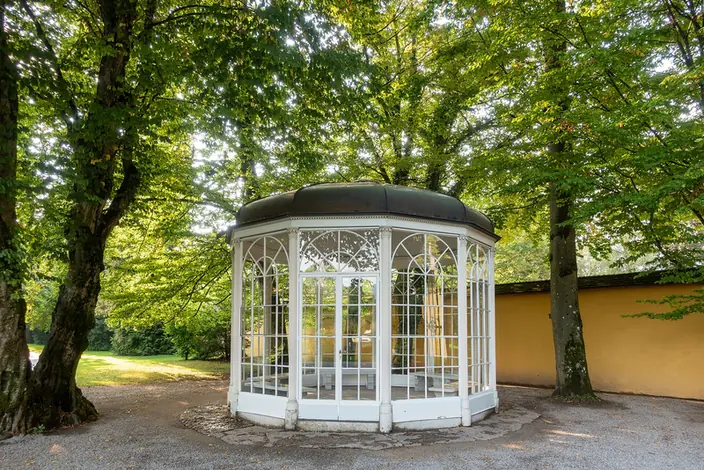The glass Sound of Music gazebo under the trees in the park of Hellbrunn Palace