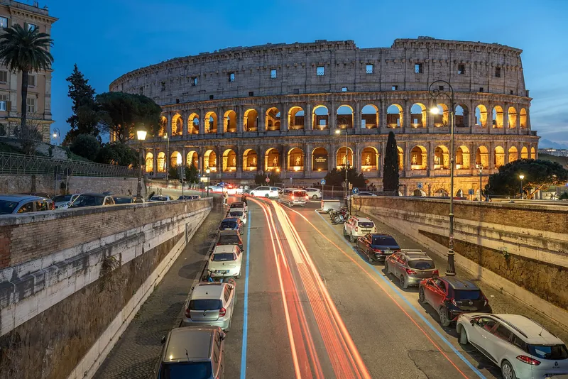 Evening traffic on Via degli Annibaldi leading to the lit Colosseum in Rome